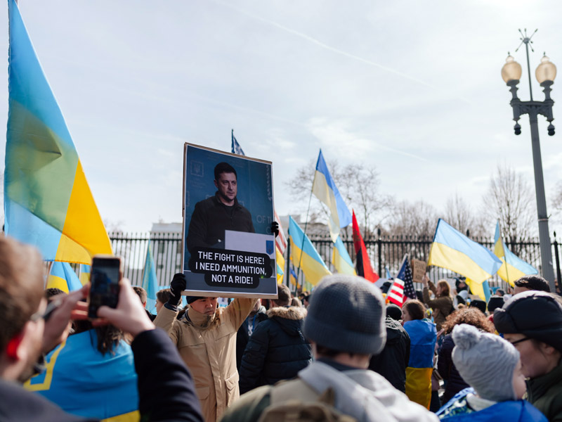 Photo of People Protesting the Ukraine-Russia War. One Protester is holding a sign of zelensky saying: I need ammunition not a ride.