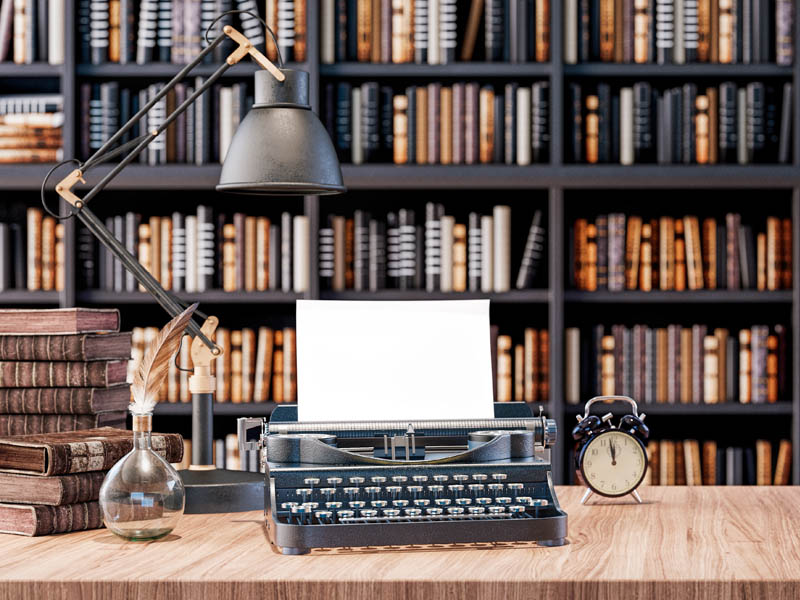 Image of Typewriter, lamp, and alarm clock on a wooden desk in a library
