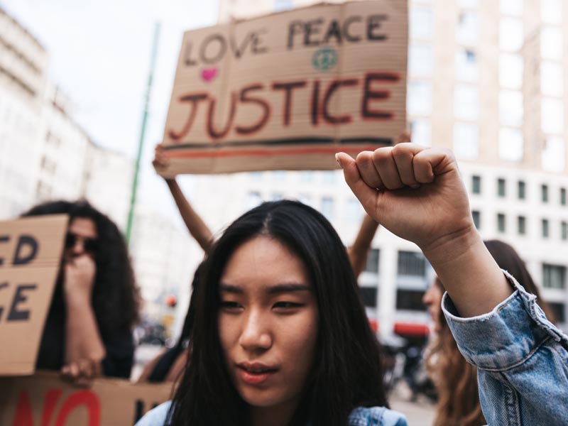 Female protestor holding a sign saying Love Peace Justice.