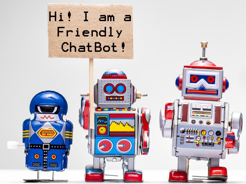 3 toy robots. 1 is holding a sign saying, "Hi! I am a Friendly ChatBot!"