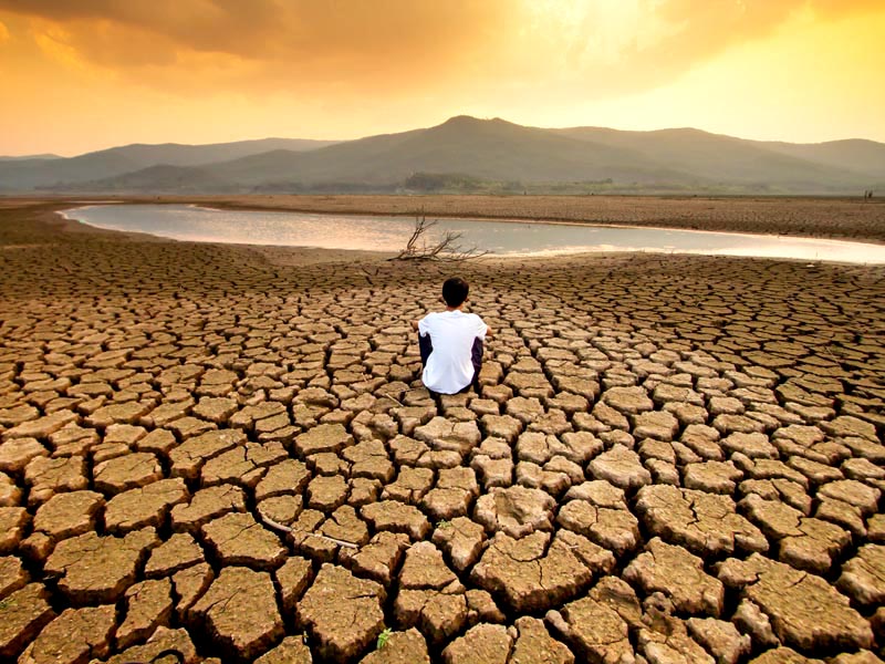 Photo of dried up lake bed with a person crouching before the remaining shoreline.